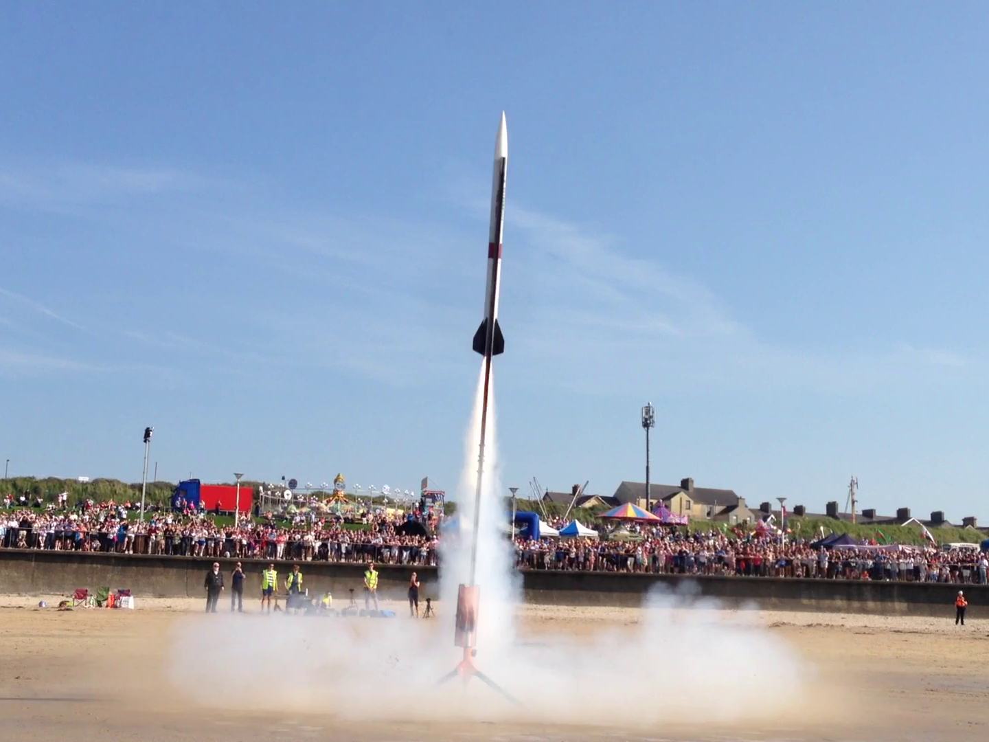 Model rocket launching with large crowd in background